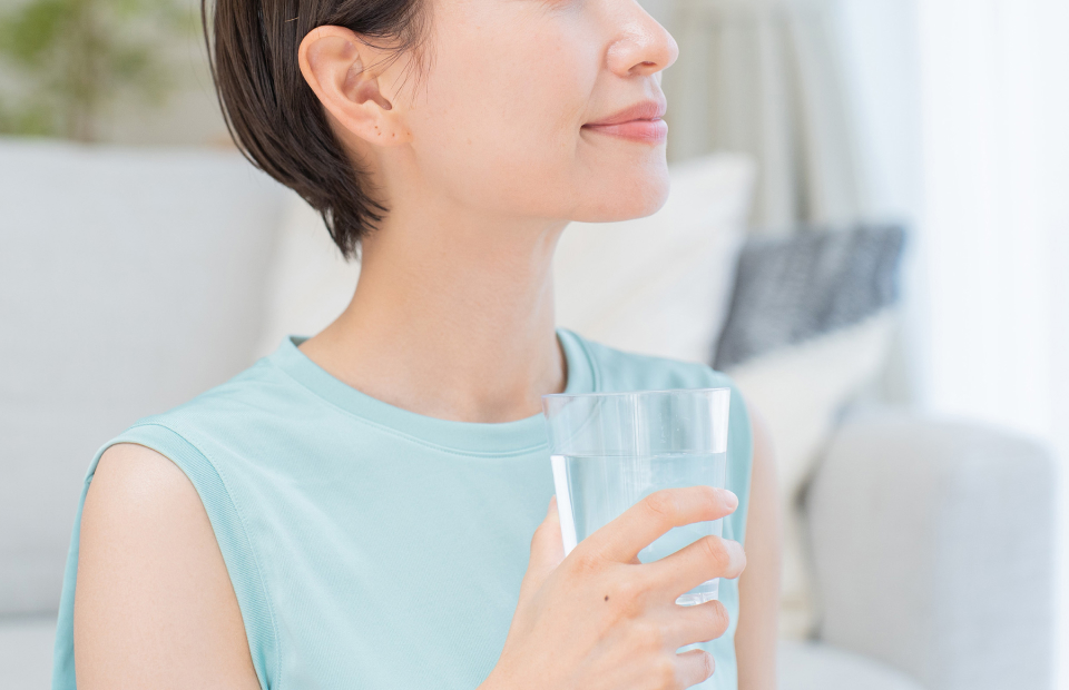 グラスの水を手に持ち、微笑む女性の上半身のアップ